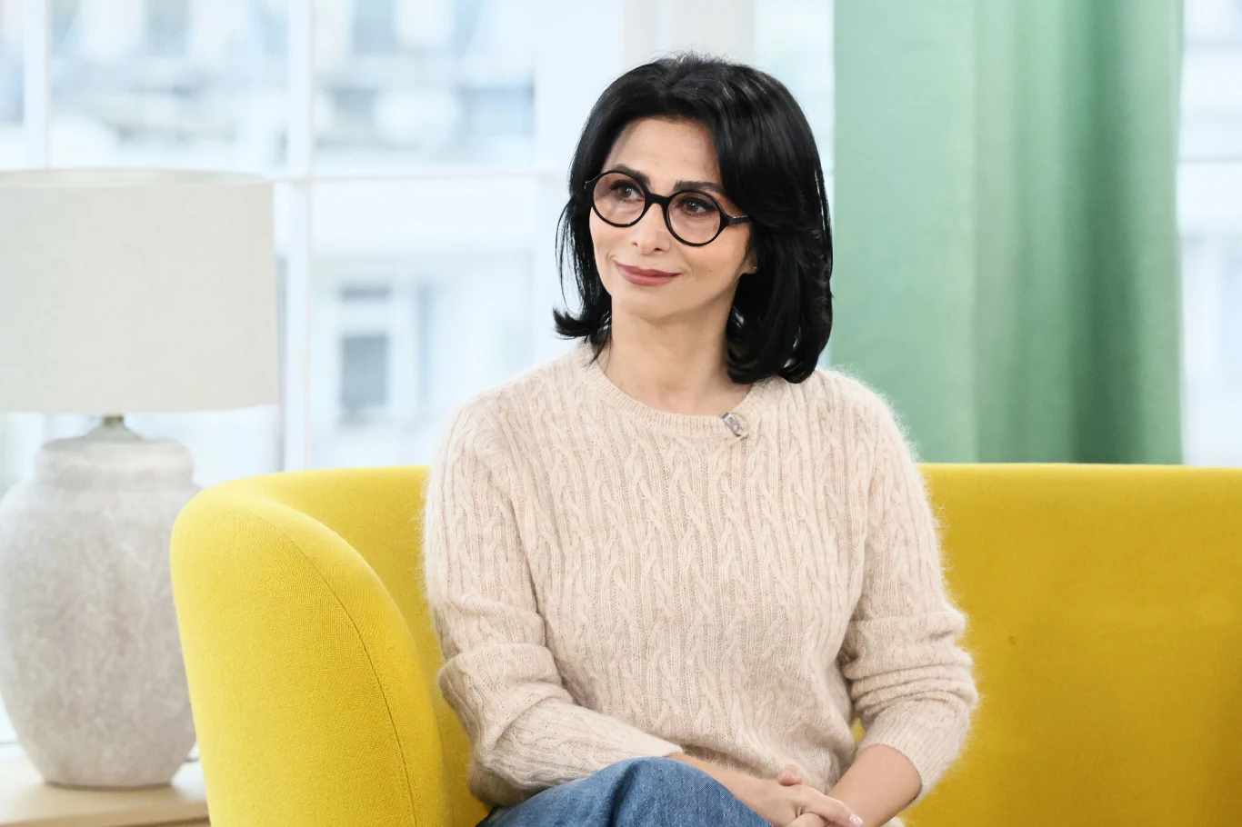 Aida Kosojan-Przybysz swój dar posiada od dziecka Kobieta z ciemnymi włosami i okularami siedzi na żółtej sofie, ubrana w jasny sweter i niebieskie spodnie, za nią znajduje się lampa oraz zielona zasłona.