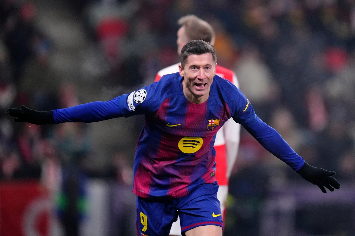 Piłkarz FC Barcelony cieszący się ze zdobytego gola podczas meczu piłkarskiego, noszący niebiesko-granatową koszulkę z numerem 9 na tle rozmytego stadionu i innych zawodników.