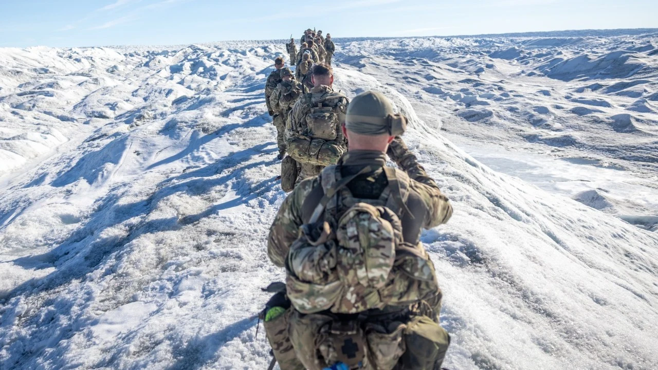 Duńscy żołnierze otrzymali rozkaz obrony Grenlandii Szereg żołnierzy w mundurach oraz pełnym wyposażeniu przemierza zaśnieżony teren górzysty, poruszając się jeden za drugim po wąskim grzbiecie lodowca pod jasnym, niebieskim niebem.