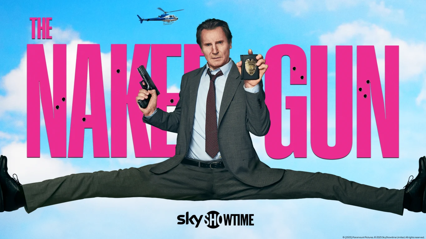 Mężczyzna w garniturze wykonuje imponujący szpagat, trzymając w jednej ręce odznakę policyjną, a w drugiej pistolet, w tle widoczny jest napis The Naked Gun na jasnym niebie oraz helikopter.