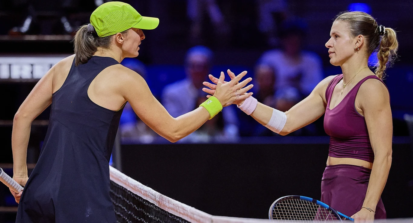 Dwie tenisistki podają sobie ręce przy siatce po zakończonym meczu, obie ubrane w sportowe stroje, jedna z nich ma jasnozieloną czapkę, druga opaskę na ramię.