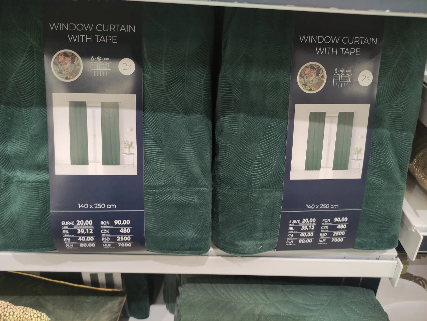 Opakowania zasłon okiennych z taśmą w intensywnym, zielonym kolorze ustawione na półce sklepowej, widoczne etykiety z wymiarami oraz cenami produktu.