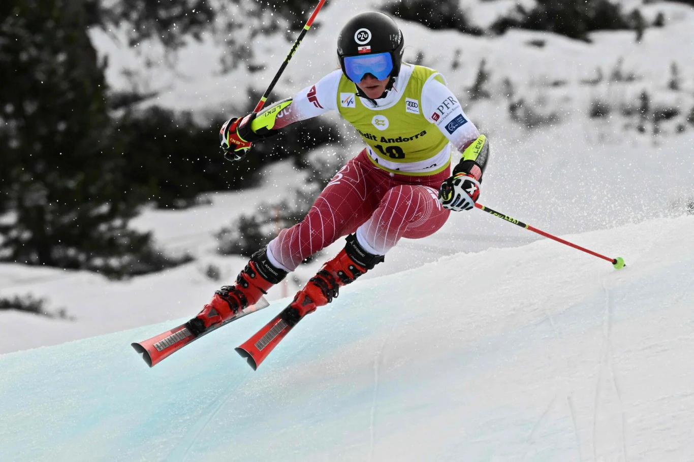 Narciarz alpejski w trakcie zjazdu, ubrany w kask i gogle, w dynamicznej pozie na śnieżnym stoku, widoczne intensywne ruchy oraz sportowa determinacja.