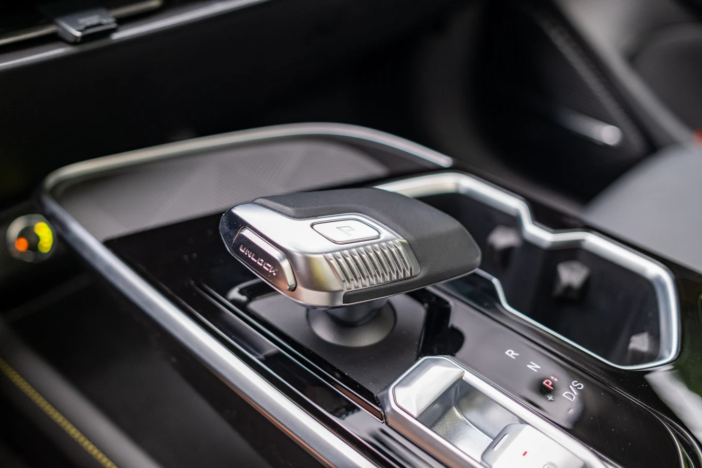 Nowoczesny joystickowy lewarek automatycznej skrzyni biegów w samochodzie, umieszczony na błyszczącym czarnym panelu środkowym z podwójnym uchwytem na napoje oraz widocznymi przyciskami zmiany trybów jazdy.