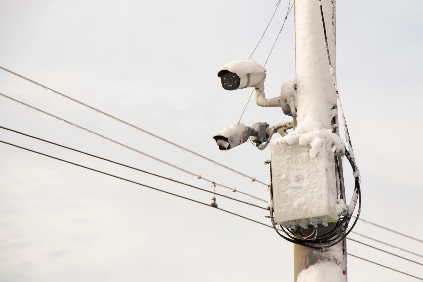 Fotoradar zasilany alkoholem ma być rozwiązaniem problemów z zasilaniem Kamery monitoringu zamontowane na słupie pokrytym śniegiem, w tle biegnące przewody elektryczne, warunki zimowe widoczne na elementach urządzenia.