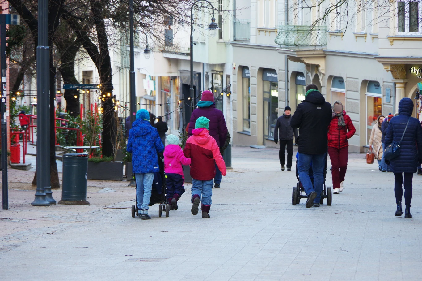 Ulga prorodzinna to najpopularniejsze odliczenie w rocznych zeznaniach podatkowych Polaków. Grupa osób spacerujących zimą po miejskim deptaku, dzieci w kolorowych kurtkach, dorośli ubrani na ciemno, część osób jedzie na hulajnogach elektrycznych, w tle fasady sklepów i nieliczne dekoracje świąteczne.