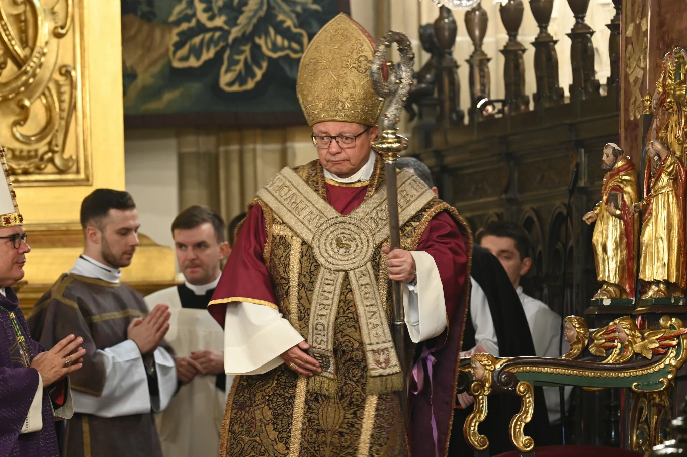 Metropolita krakowski kardynał Grzegorz Ryś Kardynał Grzegorz Ryś w liturgicznych szatach z pastorałem, w otoczeniu duchownych podczas uroczystości w kościele.