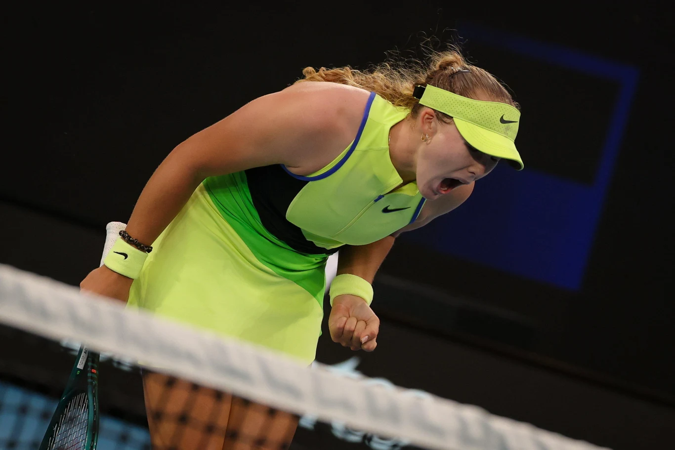 Tenisistka w jasnożółtym stroju krzyczy z emocjami na korcie, pochylona do przodu, trzyma rakietę tenisową, jej twarz wyraża silne zaangażowanie i energię podczas meczu.