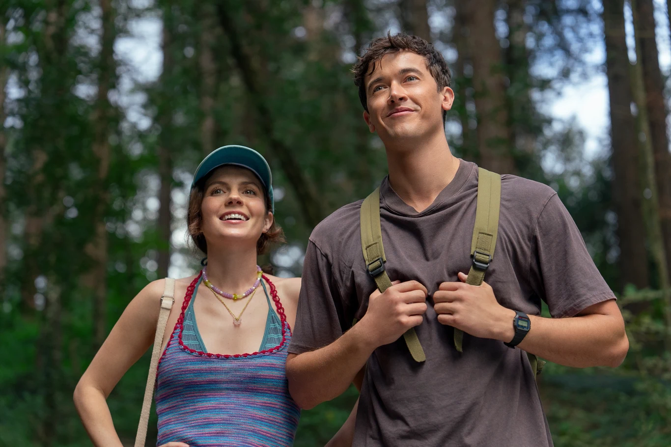 Kadr z filmu "Ludzie, których spotykamy na wakacjach" Młoda kobieta i mężczyzna w sportowych ubraniach spacerują razem po lesie, oboje wyglądają na zrelaksowanych i uśmiechniętych, a w tle widać wysokie drzewa.