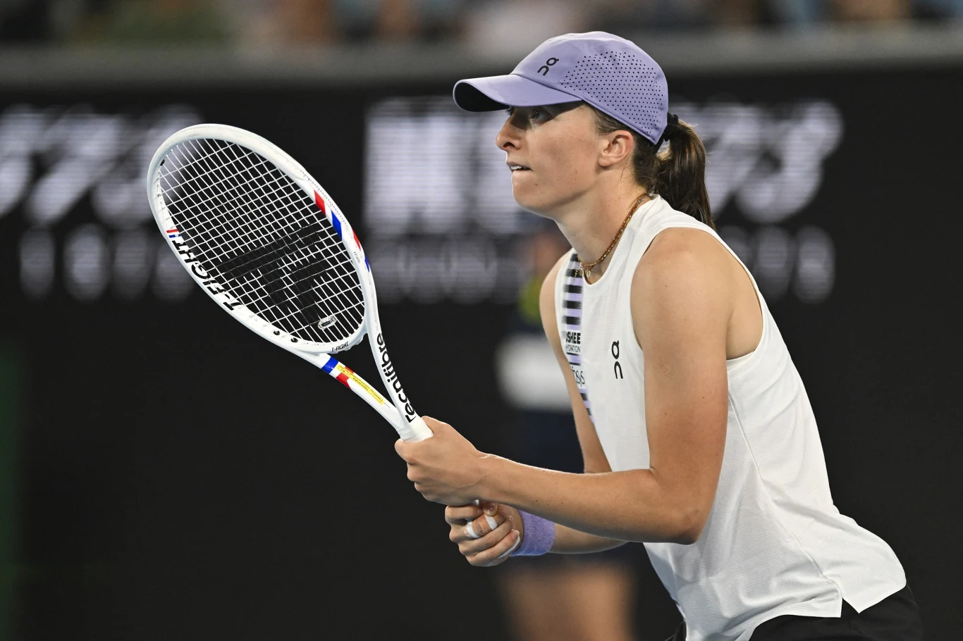 Iga Świątek rywalizowała o awans do ćwierćfinału Australian Open 2026 Zawodniczka tenisowa skupiona podczas gry na korcie, trzymająca rakietę w gotowości do odbioru piłki, ubrana w sportowy strój i fioletową czapkę z daszkiem, tło lekko rozmyte z elementami trybun.