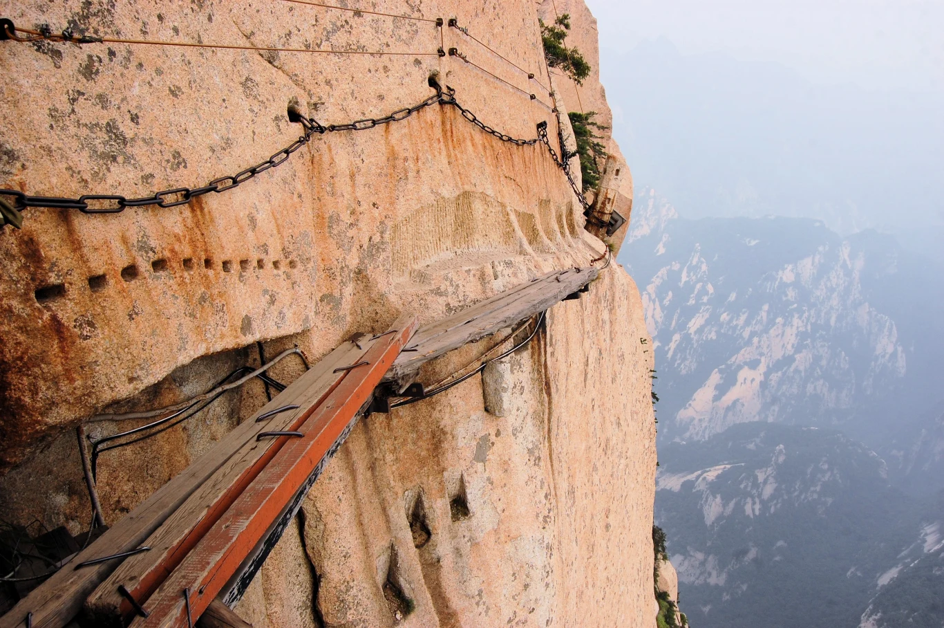 Wejście na Świętą Górę Chińczyków wymaga nie tylko silnej wiary, ale też sprawności fizycznej i odwagi Drewniana wąska kładka przymocowana do pionowej skały, zabezpieczona metalowymi łańcuchami, prowadzi wzdłuż stromego urwiska, w tle majaczą zarysy gór pokryte lekką mgłą.
