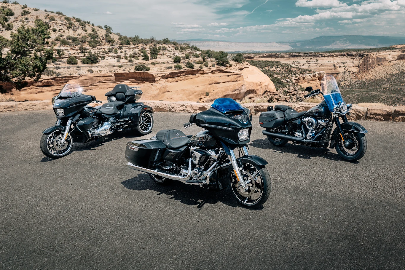 Trzy motocykle turystyczne o masywnych sylwetkach zaparkowane na asfalcie w otwartym, skalistym krajobrazie z widokiem na kaniony i rozległe niebo.