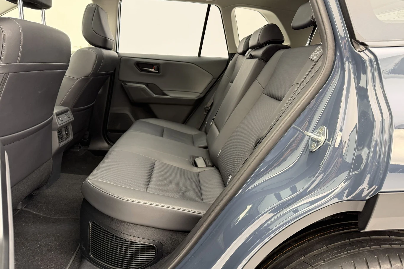 Dzięki rozmiarom nowej Toyoty RAV4 w drugim rzędzie siedzeń nie brakuje miejsca. Wnętrze tylnej części samochodu z widocznymi trzema siedzeniami, skórzaną tapicerką oraz detalami wnętrza, takimi jak wentylacja, drzwi i część oparcia foteli przednich.