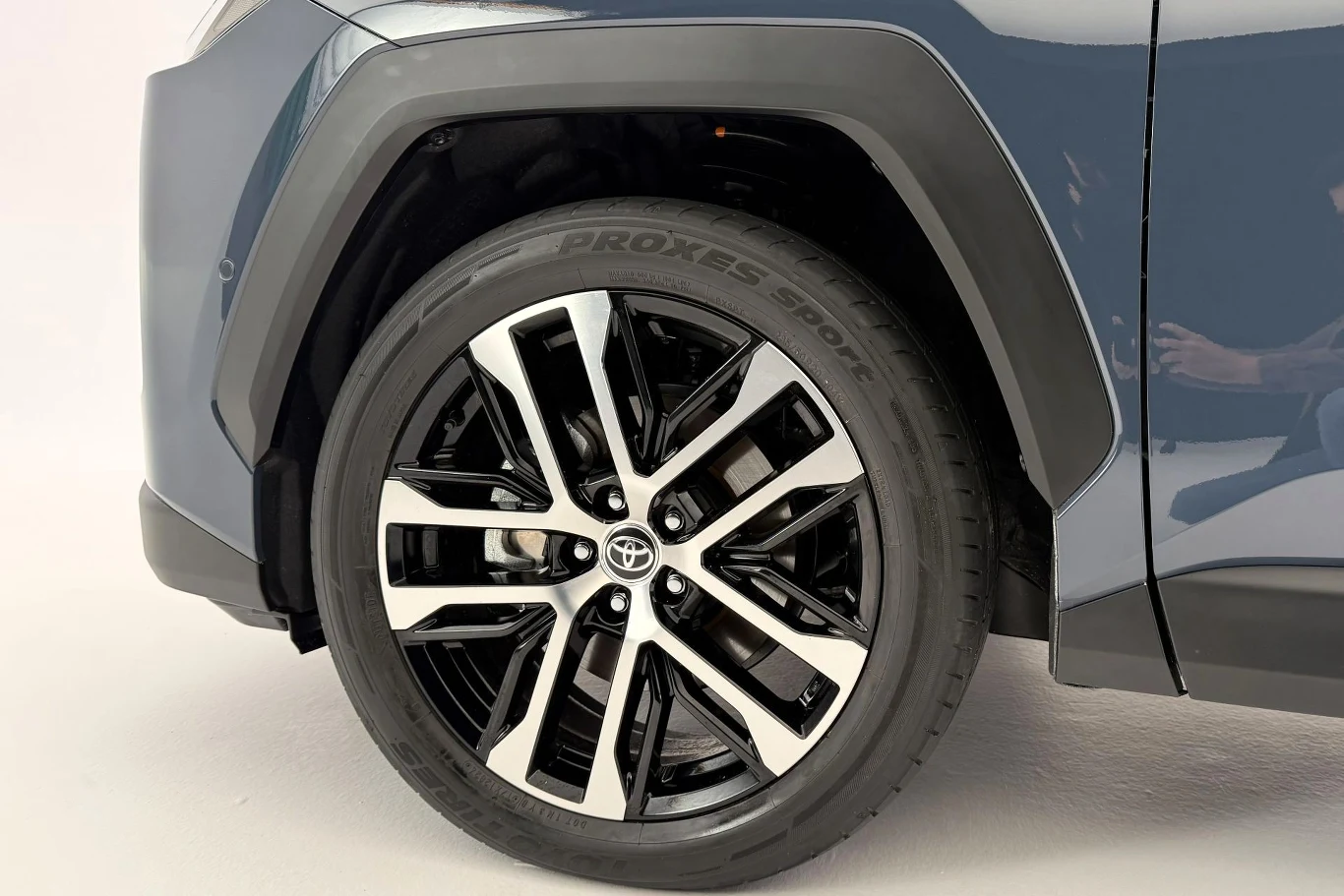 Toyota RAV4 dostępna jest z felgami w rozmiarach 18- i 20-cali w różnych wzorach (w zależności od wariantu wyposażenia). Felga aluminiowa z czarnymi i srebrnymi akcentami oraz opona marki Toyo Proxes zamontowane w przednim nadkolu niebieskiego samochodu marki Toyota.