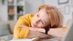 Zmęczona kobieta, leży oparta na rękach na biurku