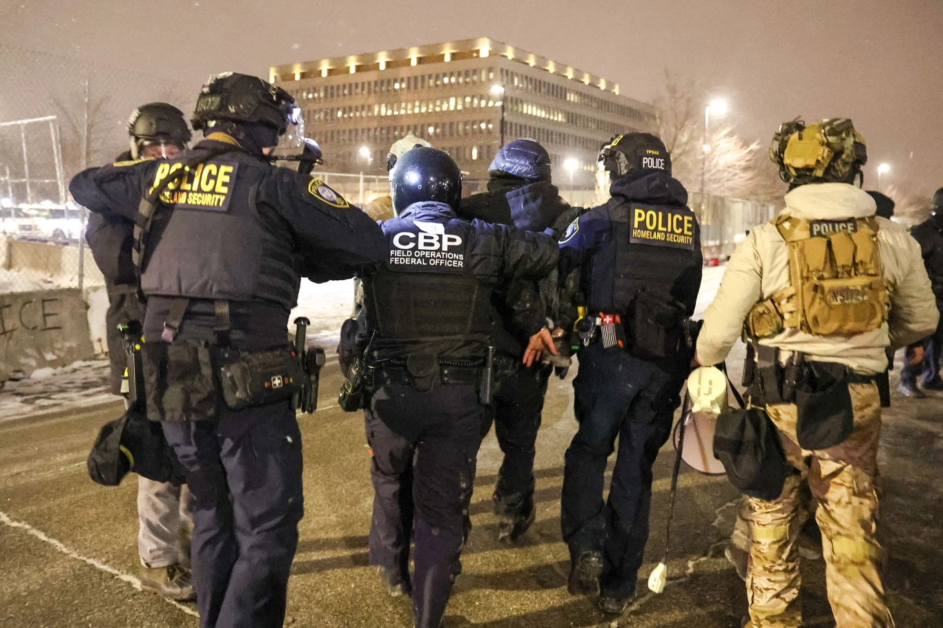 Kto odpowie za sytuację w Minneapolis? Grupa uzbrojonych funkcjonariuszy w mundurach, z wyraźnymi napisami 'POLICE' oraz 'CBP', eskortuje osobę ze skrępowanymi rękami, otoczenie miejskie oświetlone wieczornym światłem, w tle nowoczesny budynek.