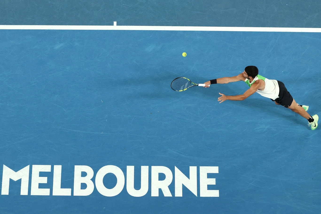 Carlos Alcaraz zameldował się w półfinale Australian Open Zawodnik tenisa ziemnego w sportowym stroju dynamicznie wyciąga się do uderzenia piłki na niebieskim korcie podczas meczu, w tle widoczne duże białe napisy MELBOURNE na korcie.