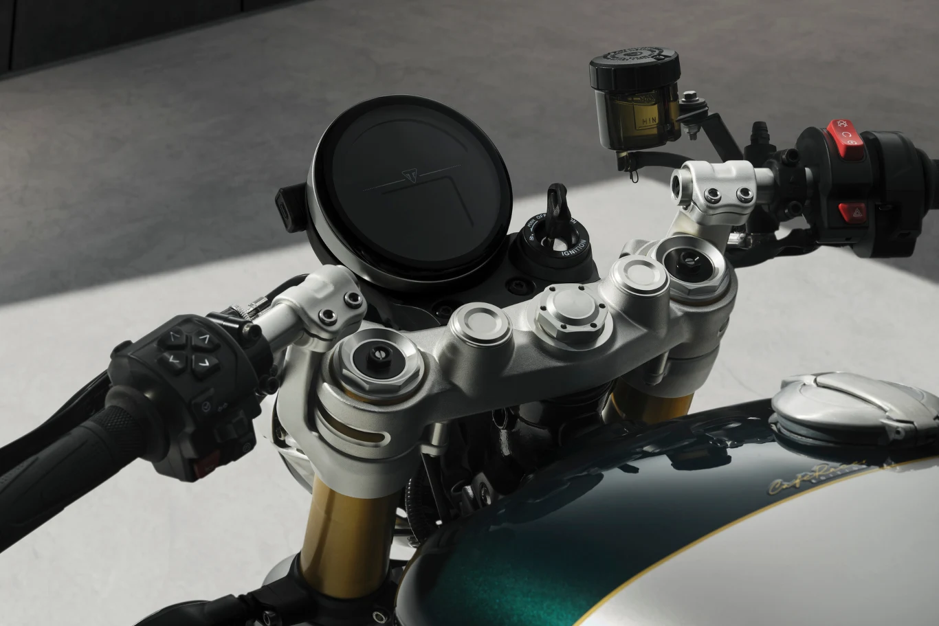 Wyświetlacz LCD oraz TFT został ukryty w klasycznej, okrągłej obudowie. Kokpit nowoczesnego motocykla z widoczną kierownicą, dźwigniami oraz wyświetlaczem cyfrowym. Złote golenie przedniego zawieszenia i stylowa zielona owiewka podkreślają sportowy charakter maszyny.