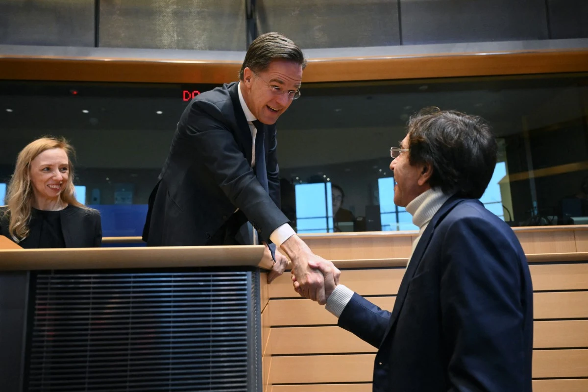 Sekretarz generalny NATO Mark Rutte w Parlamencie Europejskim Dwóch mężczyzn ściska sobie dłonie ponad barierką w przestrzeni przypominającej salę parlamentarną, obok stoi kobieta z uśmiechem obserwująca sytuację.