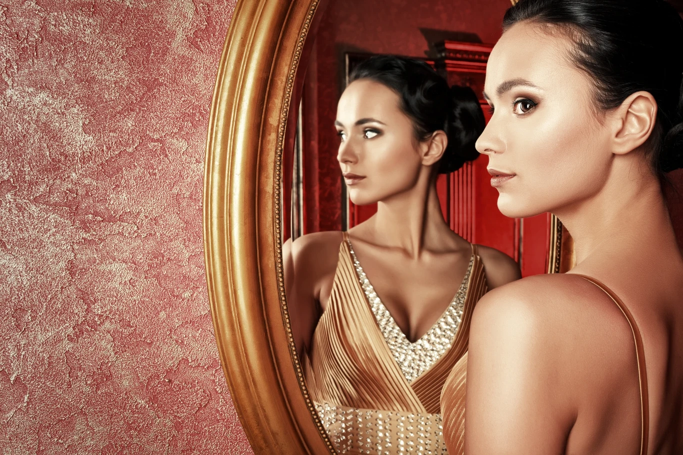 Elegancka kobieta w sukni o złotym odcieniu patrzy w lustro w stylowej, klasycznej oprawie. Delikatne światło podkreśla jej wyraziste rysy twarzy i subtelny makijaż, a tło w odcieniach różu komponuje się z całością tworząc wyrafinowaną i spokojną atmos...