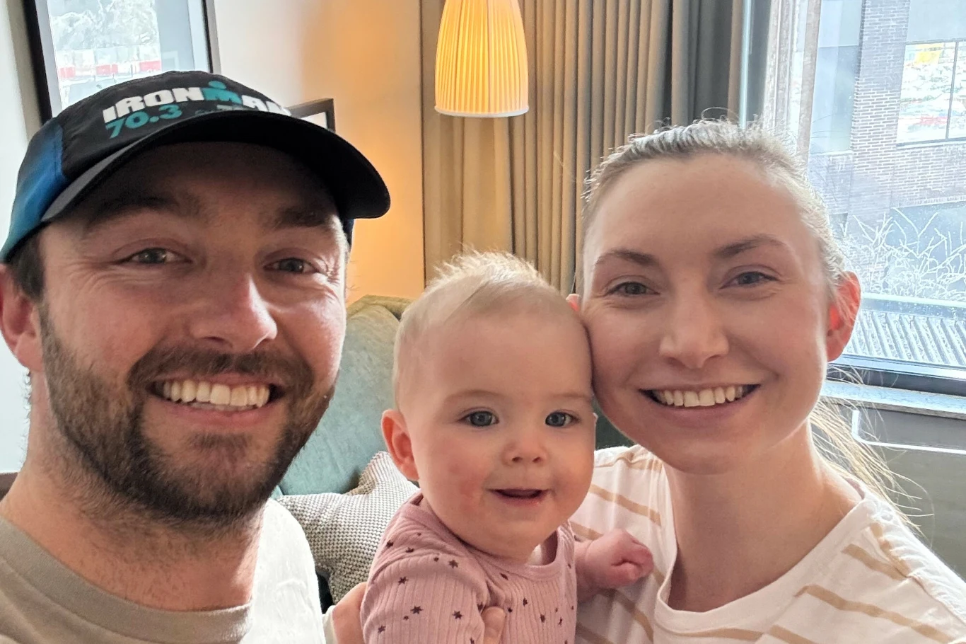 Alex Murray z żoną Mirandą i ich córką Margot przed zimą schronili się w pokoju hotelowym Młode małżeństwo z uśmiechniętym niemowlęciem w jasnym, przyjaznym salonie, za oknem widoczne miejskie zabudowania.