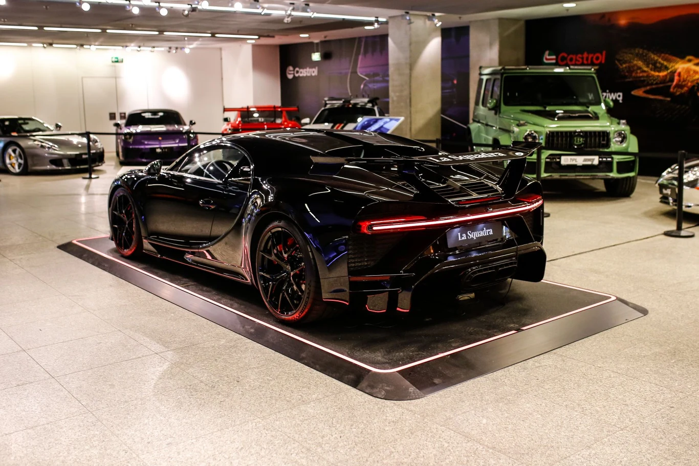 Luksusowy czarny samochód sportowy Bugatti prezentowany w nowoczesnym salonie, otoczony innymi wyjątkowymi pojazdami i wyeksponowany na podświetlonej platformie