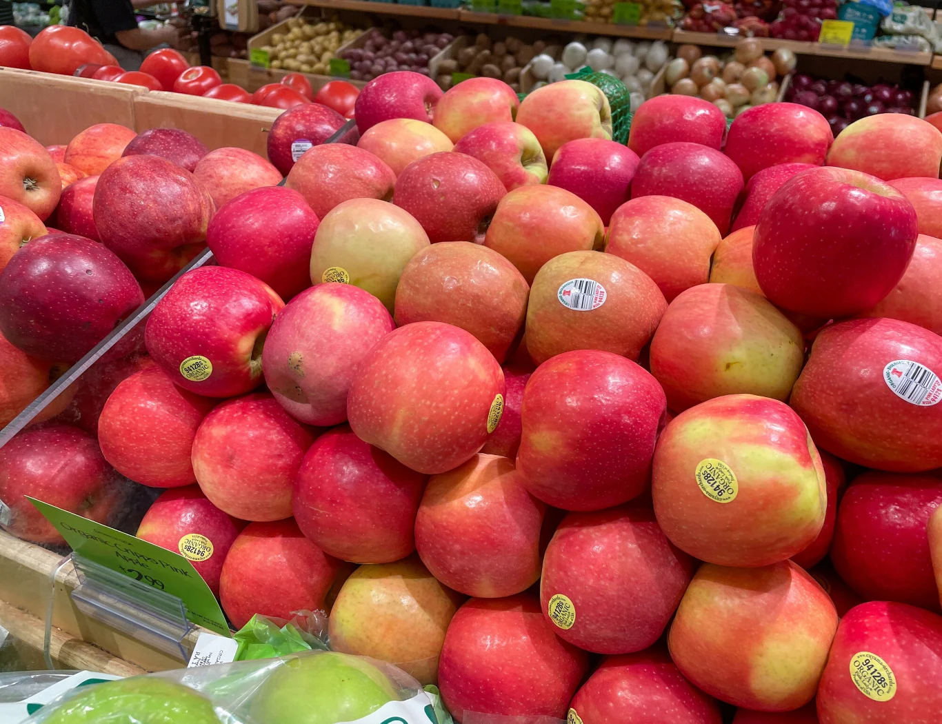 Na skrzynkach z owocami i warzywami będą pojawiały się flagi, aby klienci wiedzieli skąd pochodzą Stos jabłek w różnych odcieniach czerwieni i żółtego ułożony na stoisku w supermarkecie, w tle inne owoce oraz warzywa.