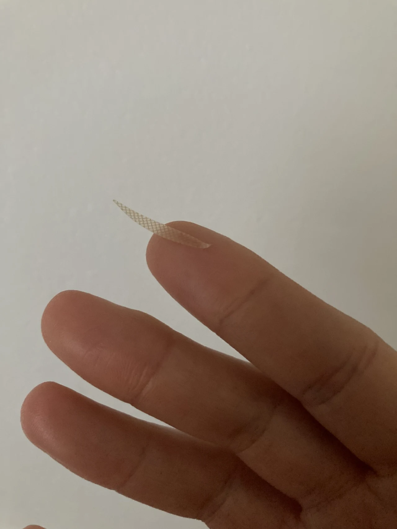 Palec wskazujący z długim, lekko wygiętym paznokciem na tle jasnej, jednolitej ściany.