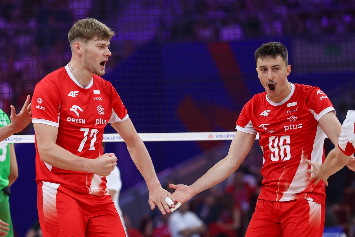 Mateusz Poręba (z lewej) Dwóch siatkarzy w czerwonych strojach reprezentacji Polski świętuje udane zagranie na boisku podczas meczu, stojąc tuż przy siatce.
