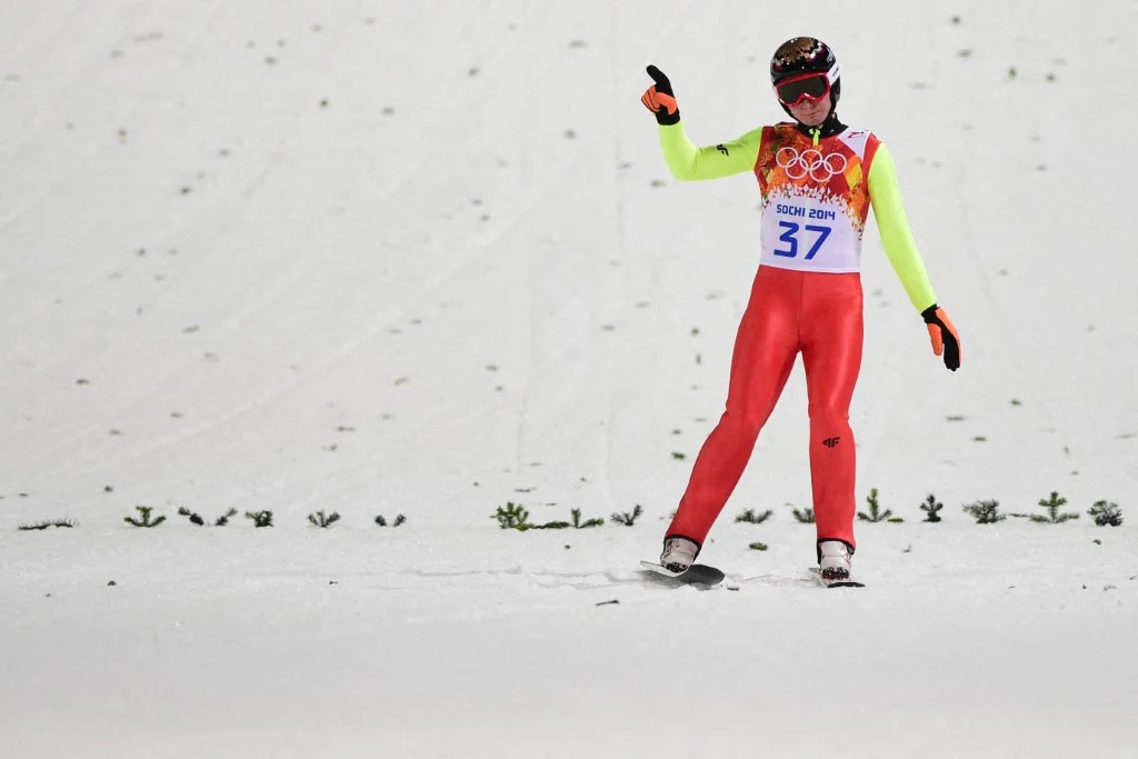 Jan Ziobro zajął 13. i 15. miejsce w konkursach indywidualnych w Soczi Zawodnik w stroju narciarskim oraz kasku i goglach, startujący z numerem 37 podczas zimowych igrzysk olimpijskich, stojący na śniegu i wskazujący ręką, w tle widoczne są pojedyncze kępki trawy wystające spod śniegu.