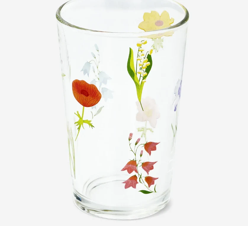 Wydano ostrzeżenie publiczne dotyczące wyrobu do kontaktu z żywnością: migracja ołowiu i kadmu z obrzeża szklanek Szklanka wykonana z przezroczystego szkła ozdobiona wielokolorowymi motywami kwiatów, spośród których wyróżniają się mak, konwalia, żółty kwiat i czerwone liście.