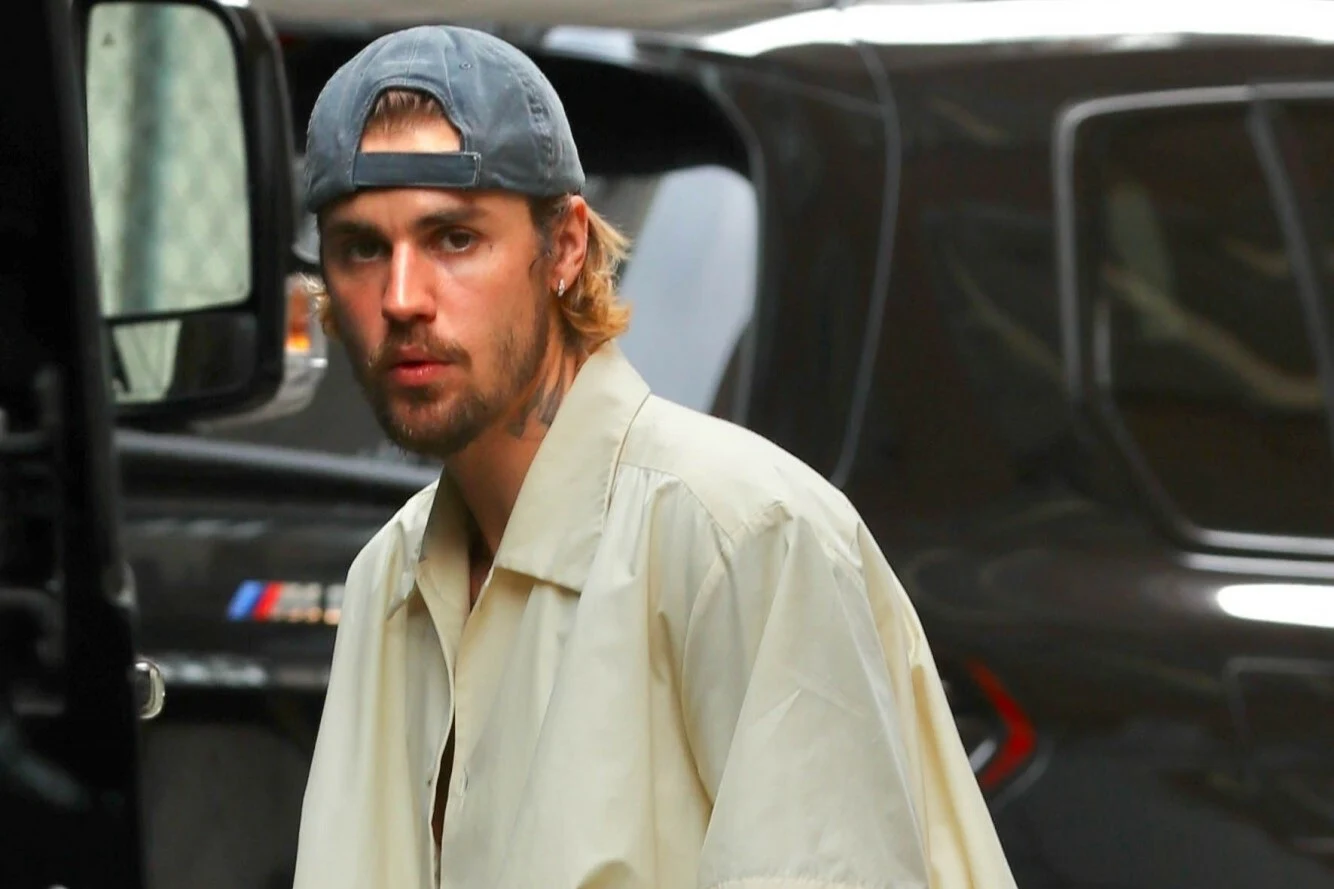 Justin Bieber wystąpi podczas tegorocznej gali Grammy Mężczyzna w jasnej kurtce i czapce z daszkiem skierowanej do tyłu stoi na tle ciemnego samochodu, patrząc w stronę aparatu. Ma zarost i dłuższe włosy, a jego wyraz twarzy jest neutralny.