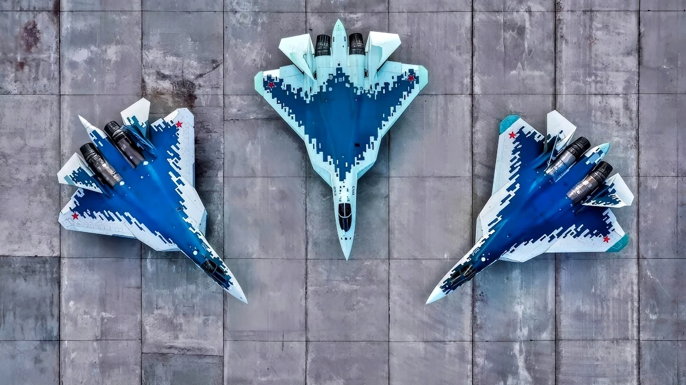 Ukraińcy zniszczyli rosyjskie samoloty i radary warte 15 miliardów dolarów Trzy nowoczesne myśliwce o charakterystycznym kształcie skrzydeł i niebiesko-białym malowaniu stoją w symetrycznym układzie na betonowej płycie lotniska, widziane z lotu ptaka.