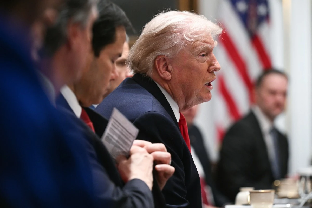 Iran szykuje odpowiedź na rozszerzone sankcje Stanów Zjednoczonych. Prezydent USA przy stole konferencyjnym, w garniturze i czerwonym krawacie, z flagą USA w tle.