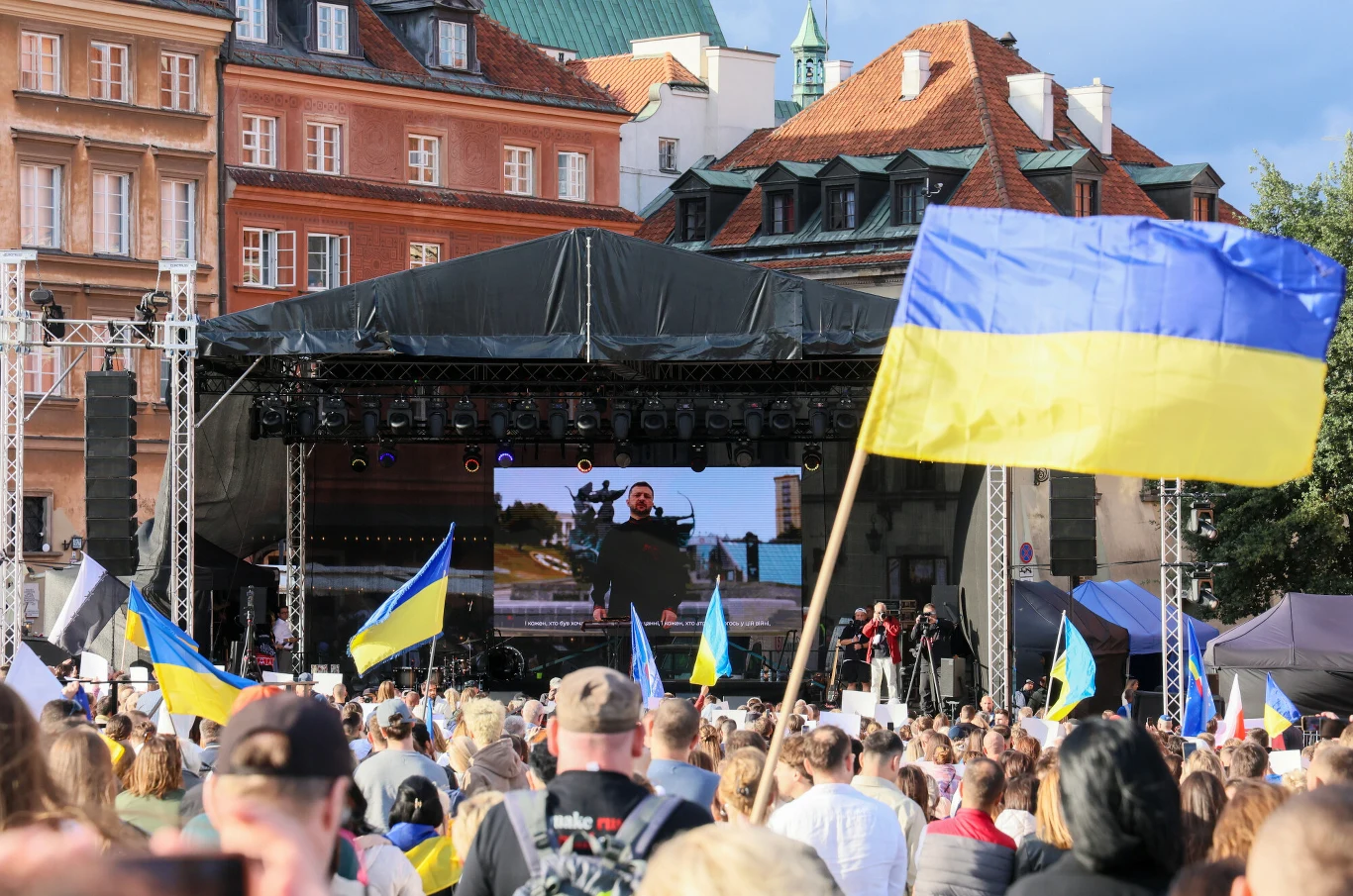 Sondaż. Zapytali Ukraińców, co sądzą o Polakach. Oto, co odpowiedzieli Tłum ludzi zgromadzony przed sceną plenerową w centrum miasta, na scenie wyświetlany jest ekran z osobą przemawiającą, liczne flagi Ukrainy powiewają wśród uczestników, w tle zabytkowe budynki.