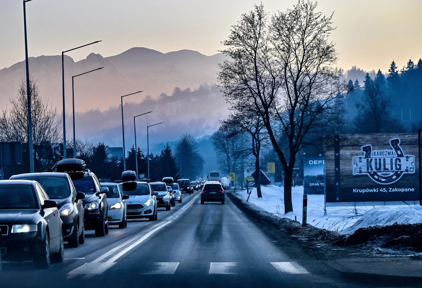 Według danych przekazanych przez Generalną Dyrekcję Dróg Krajowych i Autostrad, w ciągu pierwszych dwóch tygodni ferii zimowych tunelem na drodze ekspresowej S7 przejechało blisko 400 tys. samochodów. Ruch samochodowy na drodze prowadzącej przez zaśnieżony krajobraz z widocznymi górami w tle, po prawej stronie widoczny billboard reklamowy, drzewa bez liści oraz zimowa sceneria.