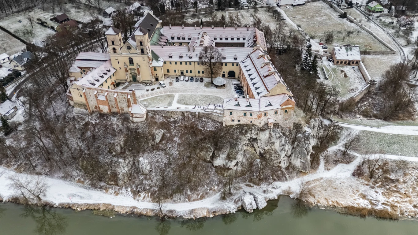 Duży kompleks zabudowań klasztornych na skale nad rzeką, pokryty śniegiem. W tle zimowy krajobraz z polami i drzewami.