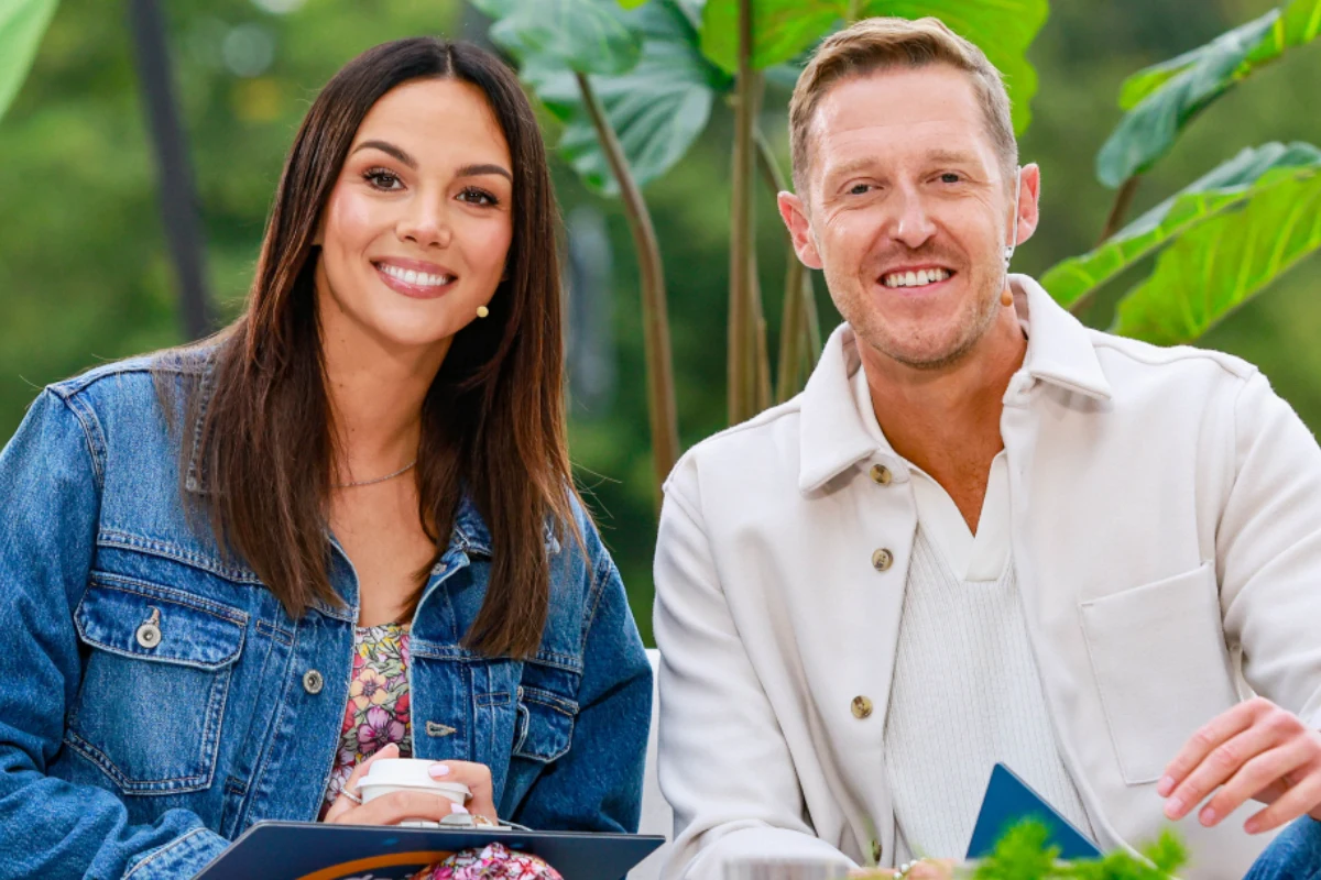 Paulina Krupińska i Damian Michałowski Dwoje uśmiechniętych dorosłych siedzi obok siebie w jasnych ubraniach, w tle znajdują się zielone rośliny i rozmyte elementy natury.