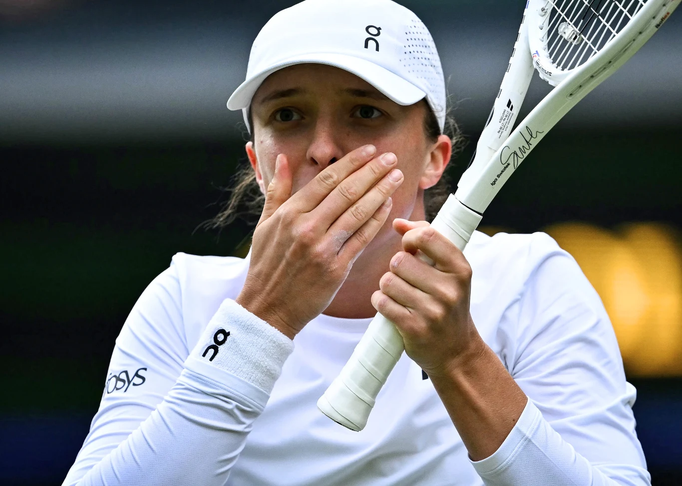 Iga Świątek - obecna wiceliderka rankingu WTA Tenisistka w białym stroju i czapce trzyma rakietę z widocznym pękniętym naciągiem oraz zasłania dłońmi usta, wyrażając zaskoczenie lub niedowierzanie.