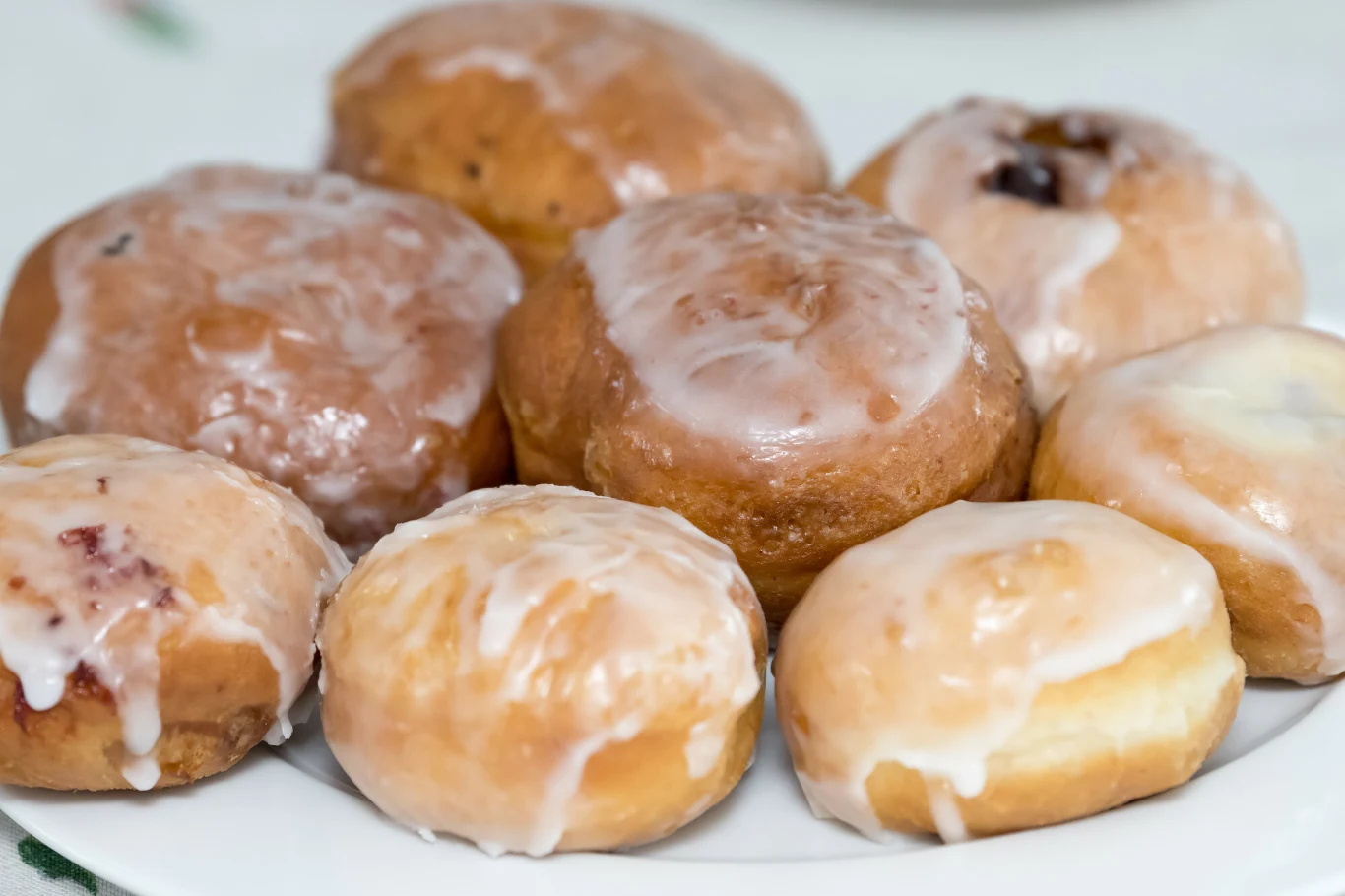 12 lutego klienci ruszą szturmem na cukiernie. U Magdy Gessler z pewnością będą ustawiać się długie kolejki Talerz z ośmioma pączkami obficie polanymi lukrem, każdy o okrągłym kształcie i delikatnie złocistej powierzchni. Pączki różnią się wielkością, a ich błyszczący lukier sugeruje świeżość i słodycz wypieku.