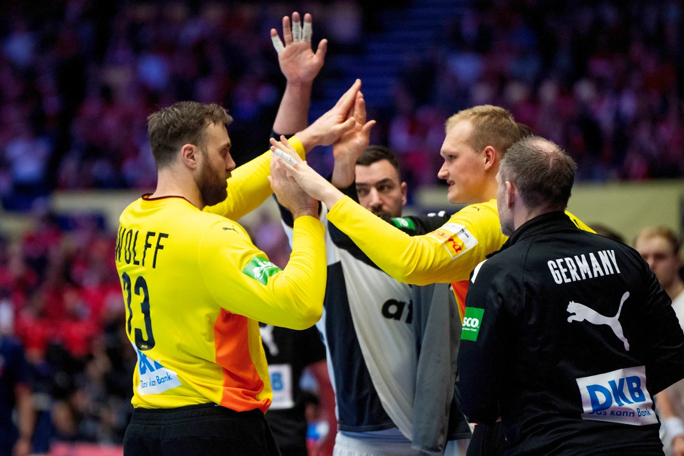Andreas Wolff (z lewej) Zawodnicy drużyny piłki ręcznej w żółto-czarnych strojach przybijają sobie piątki podczas meczu, w tle widać trybuny z kibicami i innych uczestników spotkania.