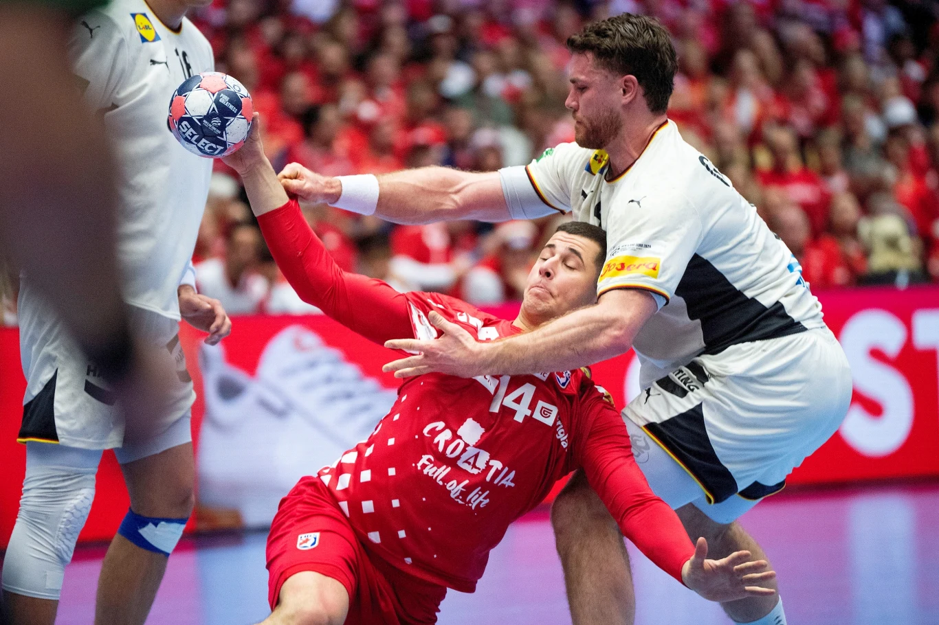 Mecz Niemcy - Chorwacja wyłonił pierwszego finalistę mistrzostw Europy Zawodnik w czerwonym stroju z numerem 14 z drużyny Chorwacji walczy o piłkę z rywalem w białym stroju, obaj są zaangażowani w intensywny kontakt fizyczny na boisku otoczonym przez widownię w tle.