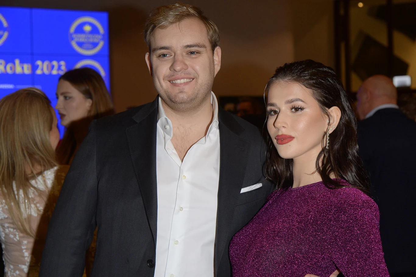 Kevin Mglej przeszedł metamorfozę Para elegancko ubranych osób pozuje razem podczas oficjalnego wydarzenia, w tle widoczne są inne osoby i wyświetlany na ekranie napis wskazujący na uroczystość lub galę.