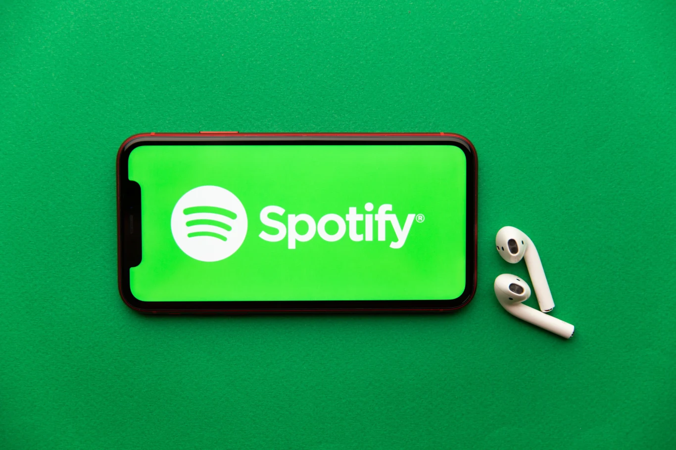 Spotify podwyższyło Polakom ceny subskrypcji Telefon z widocznym logo Spotify na ekranie, położony na zielonym tle, obok leżą białe bezprzewodowe słuchawki douszne.