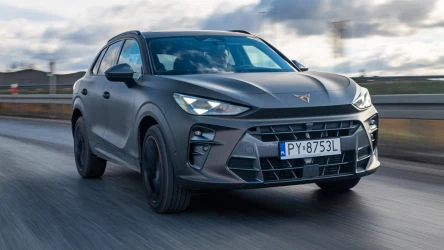 Nowoczesny samochód typu SUV w ciemnym kolorze porusza się dynamicznie po asfaltowej drodze, tło jest lekko rozmyte, co podkreśla ruch pojazdu, a rejestracja z przodu wskazuje na polskie pochodzenie.