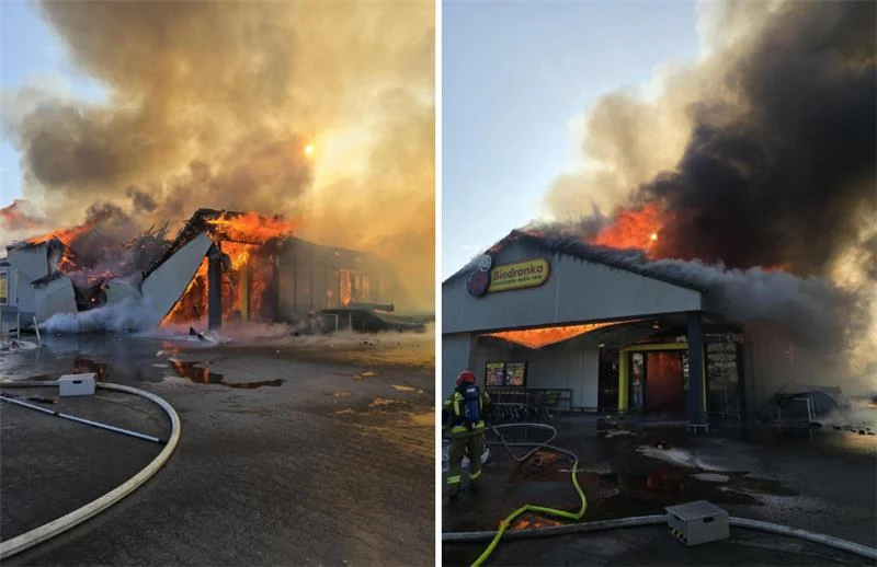 Pożar sklepu Biedronka w Polkowicach Budynek ogarnięty płomieniami, z dachu i wnętrza wydobywają się gęste kłęby dymu. Przed budynkiem stoją strażacy, którzy prowadzą akcję gaśniczą. Przed lokalem rozciągnięte są węże strażackie, a otoczenie pokryte jest wodą i sadzą.