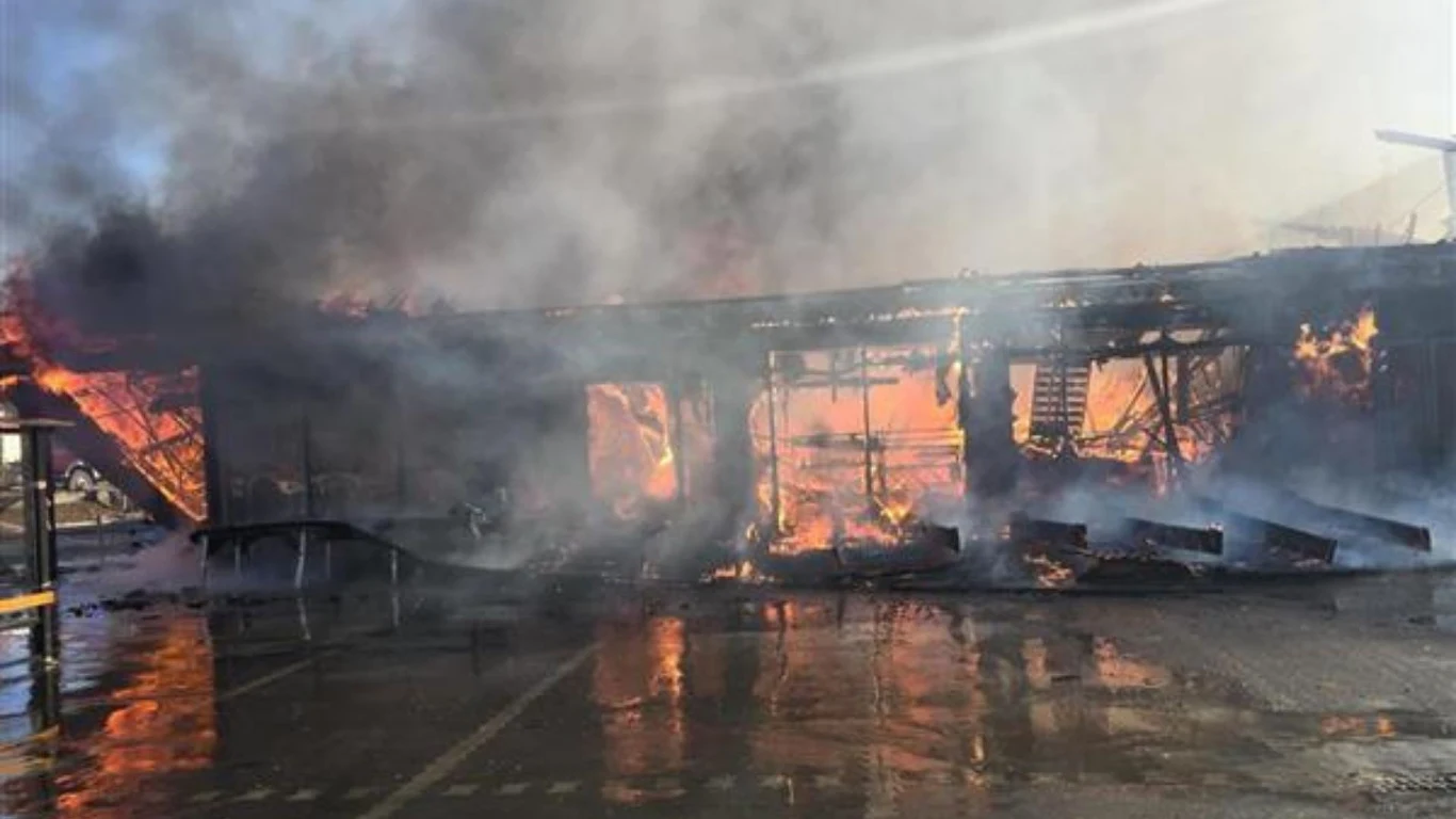 Zawalił się dach, sklep Biedronki stanął w płomieniach Ogromny pożar ogarnia budynek, płomienie wydostają się przez zawalone ściany, a całość spowita jest gęstym, ciemnym dymem. Na mokrej nawierzchni odbijają się rozświetlone ogniem fragmenty konstrukcji.