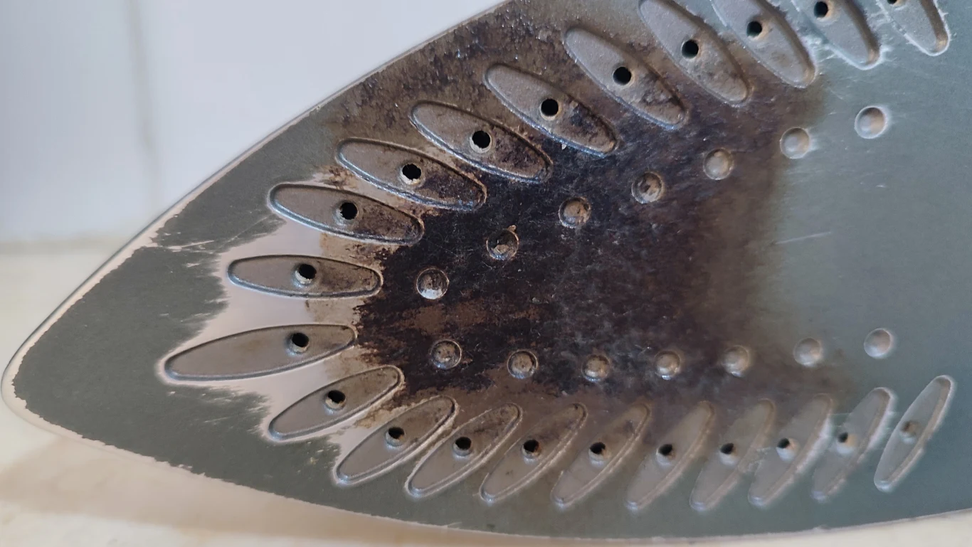 Grot żelazka z widocznymi otworami parowymi oraz śladami przypaleń na metalowej powierzchni.