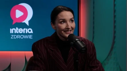 Kobieta w garniturze w pasy siedzi przy mikrofonie w studiu nagraniowym z logo 'interia ZDROWIE' w tle, uśmiecha się i prowadzi rozmowę.