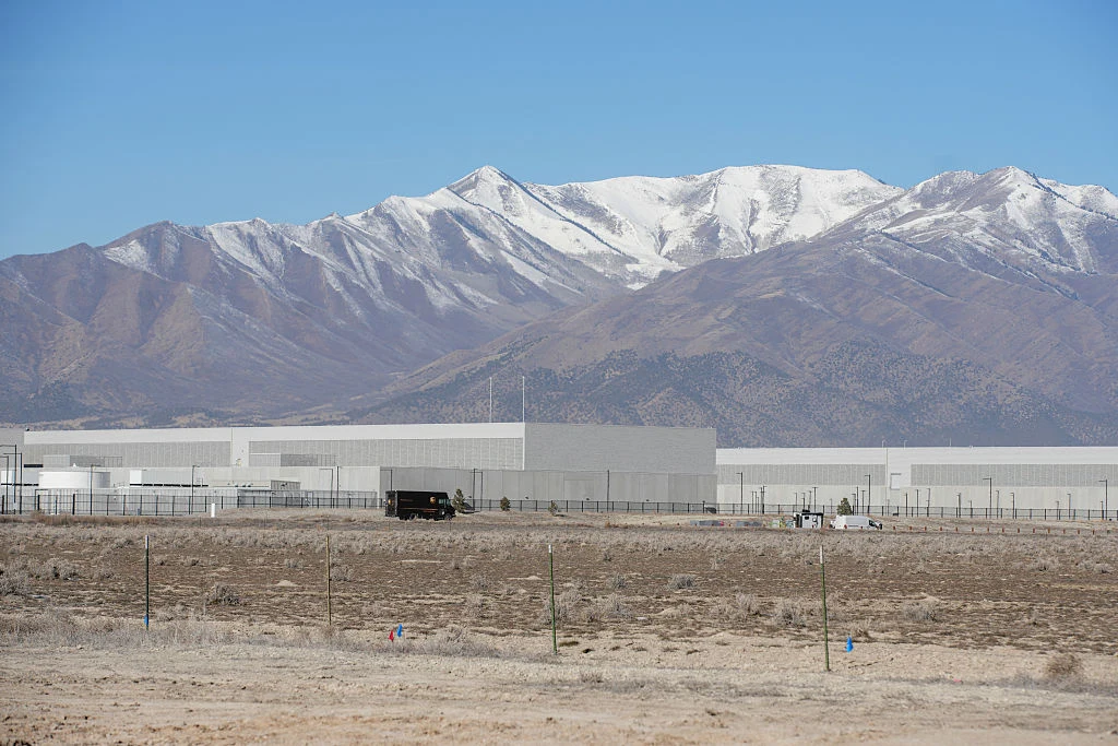 Nowoczesny kompleks przemysłowy zlokalizowany na tle zaśnieżonych gór, otoczony ogrodzeniem, w suchym, pustynnym krajobrazie.